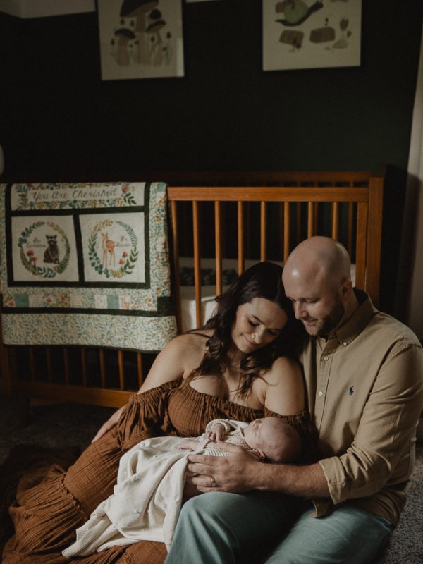 Parents sitting together and cuddling their newborn baby boy in a softly styled nursery during an in-home newborn session in Raleigh, NC. Newborn and family photography by Victoria Vasilyeva Photography.