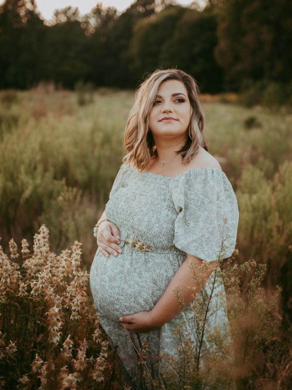 pregnant woman in flower print maxi dress staying among high grass in wake forest, nc